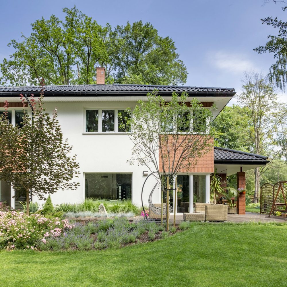 Flowers and trees in the garden of white house with windows duri