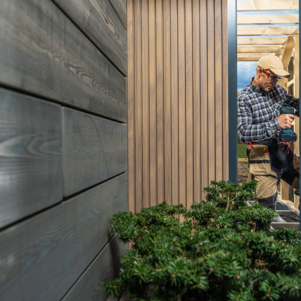 Modern Custom Garden Shed Building Performed by Caucasian Construction Worker in His 40s. Window Installing. Small Architecture Theme.